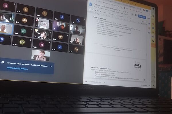 Das Foto zeigt einen Computerbildschirm, auf welchem eine Seite des Protokolls der StuRa-Sitzung sowie die Videokonferenz der Sitzung zu sehen ist.