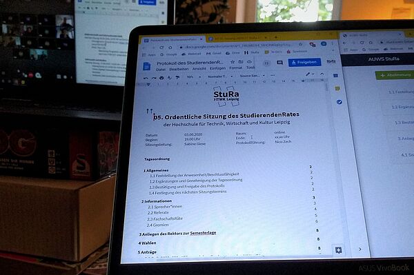 Das Foto zeigt einen Computerbildschirm, auf welchen die erste Seite des Protokoll der StuRa-Sitzung zu sehen ist. Dahinter ist auf einen zweiten Bildschirm die Videokonferenz der Sitzung zu sehen.